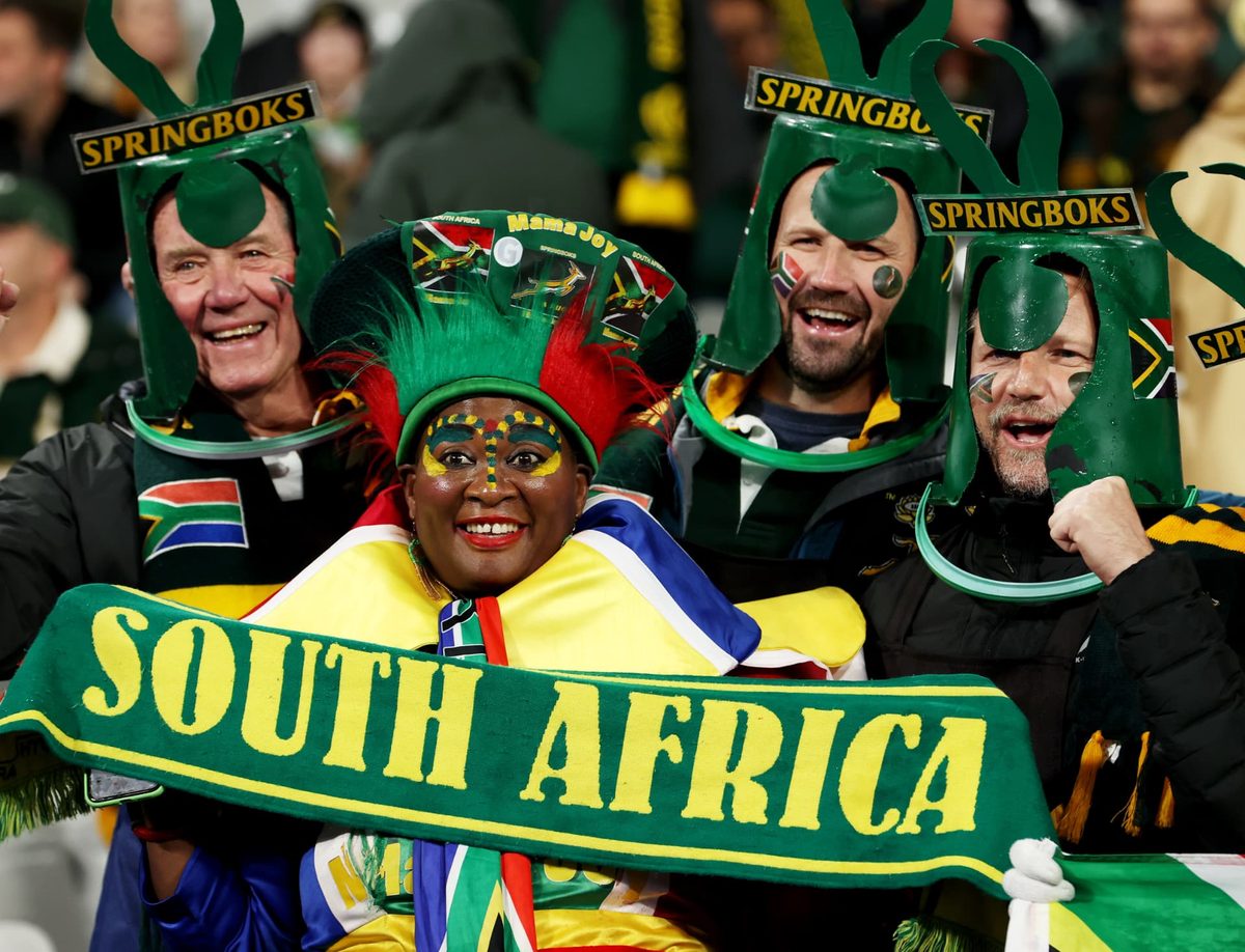 Springbok fans in supporter hard hats celebrating with a South Africa scarf